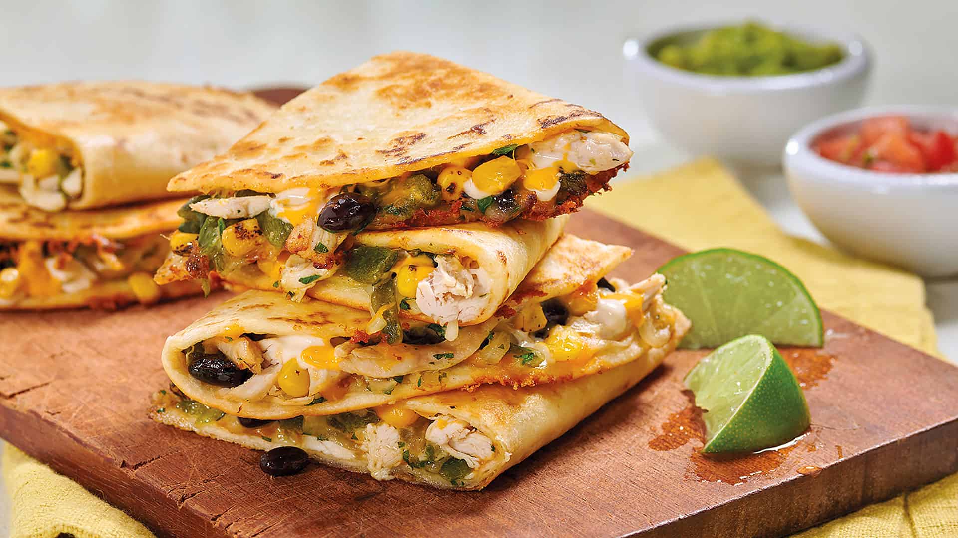 Crispy chicken and vegetable quesadillas with melted cheese served on a wooden board, garnished with lime wedges, ideal for Mexican cuisine lovers.